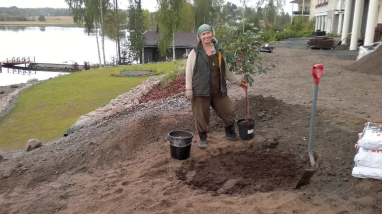 nainen istuttaa puuta järven rannalla